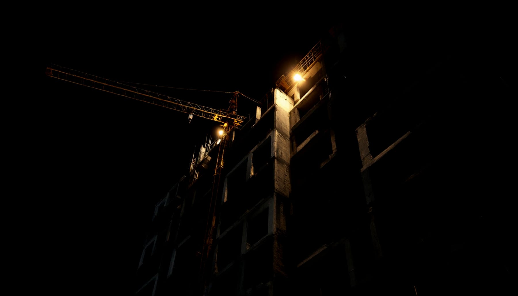 A high-rise under construction at night, lit by a single work lamp.